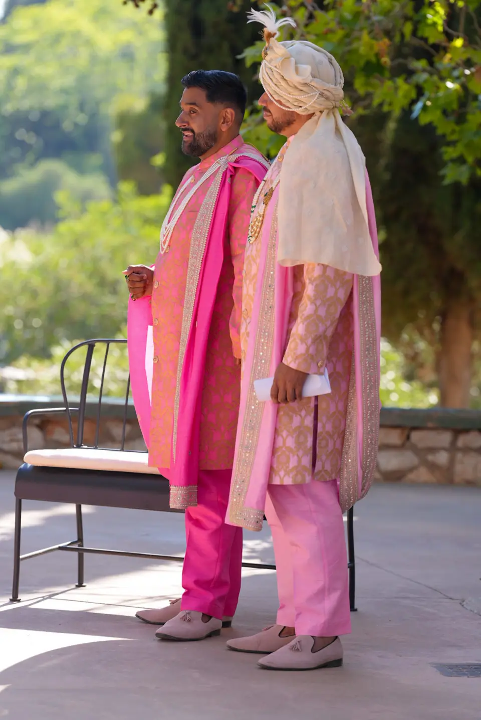 Two wedding guests in coordinated pink formalwear standing in an outdoor ceremony setting