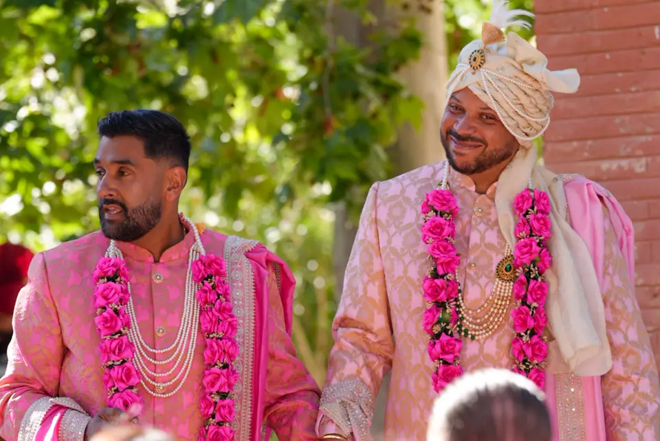 Two wedding guests in pink formalwear wearing floral garlands