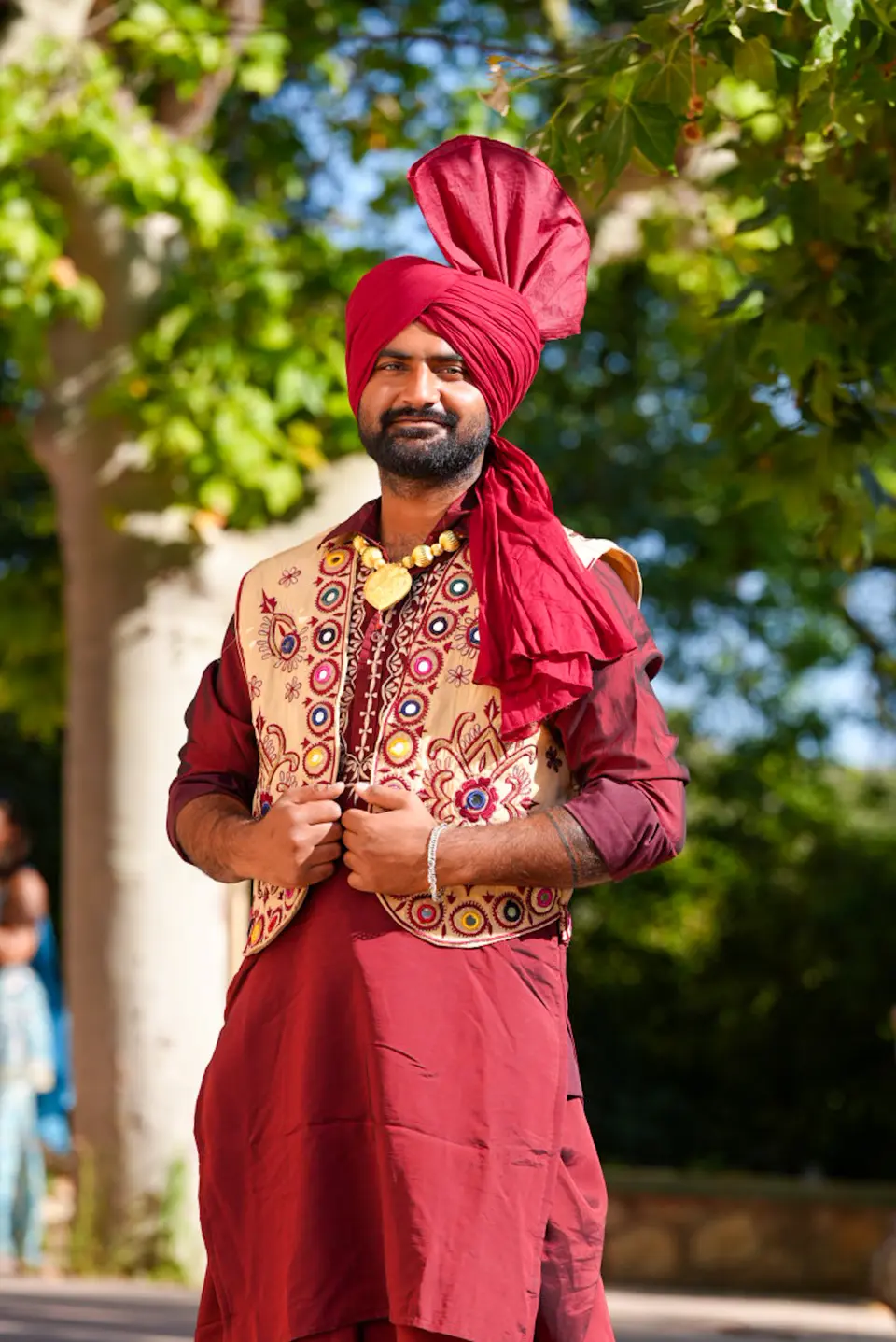 Traditional performer in a red turban standing beneath greenery